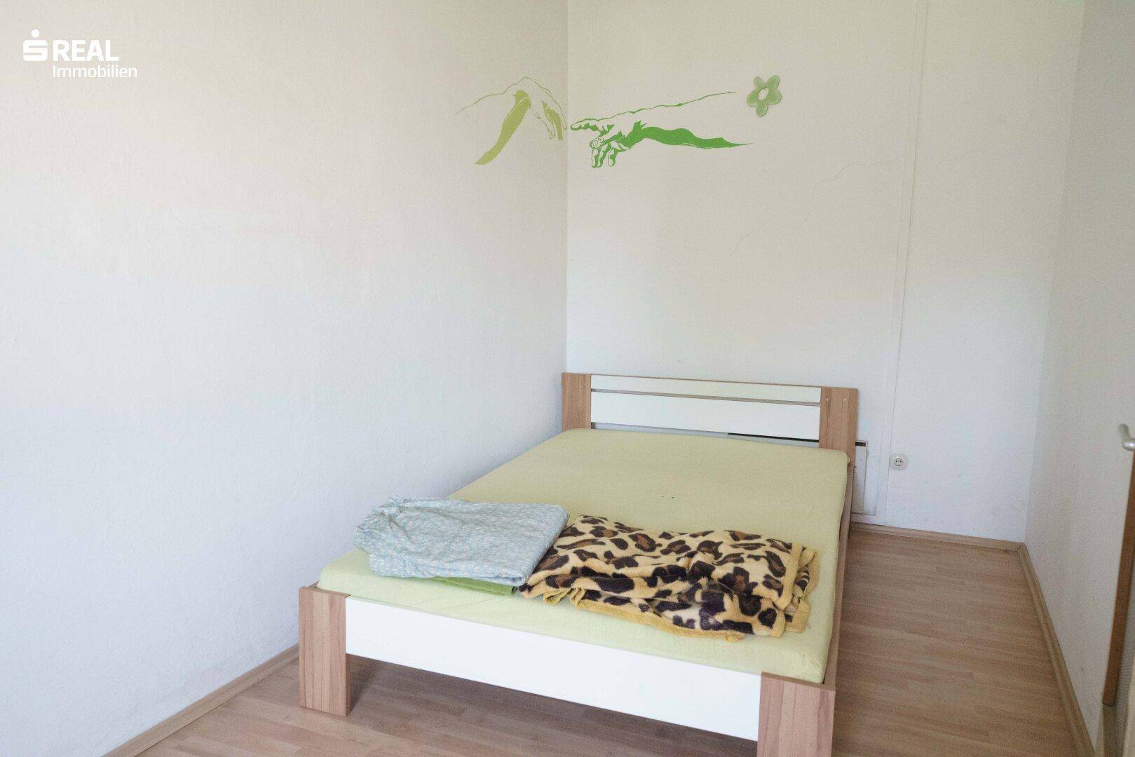 Schlafzimmer mit Einzelbett und Laminatboden, bietet eine einfache Einrichtung.