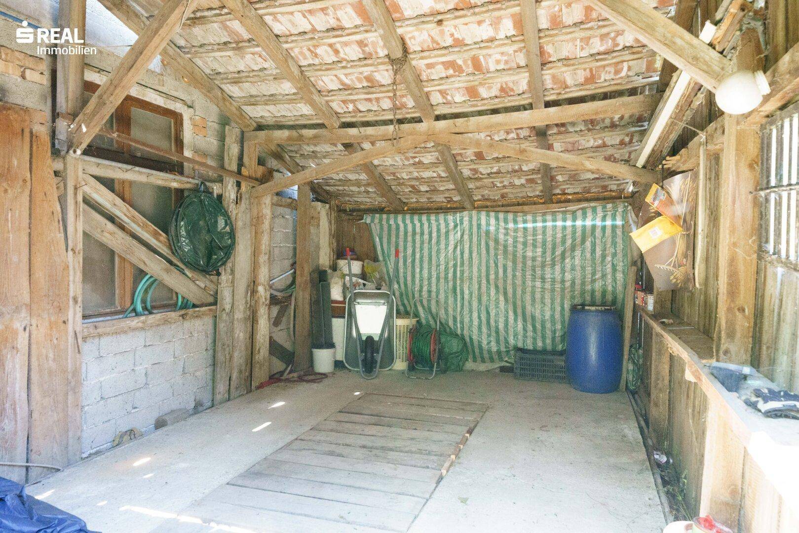 Rustikaler Innenraum eines Holzschuppens mit sichtbaren Balken und Lagerfläche.