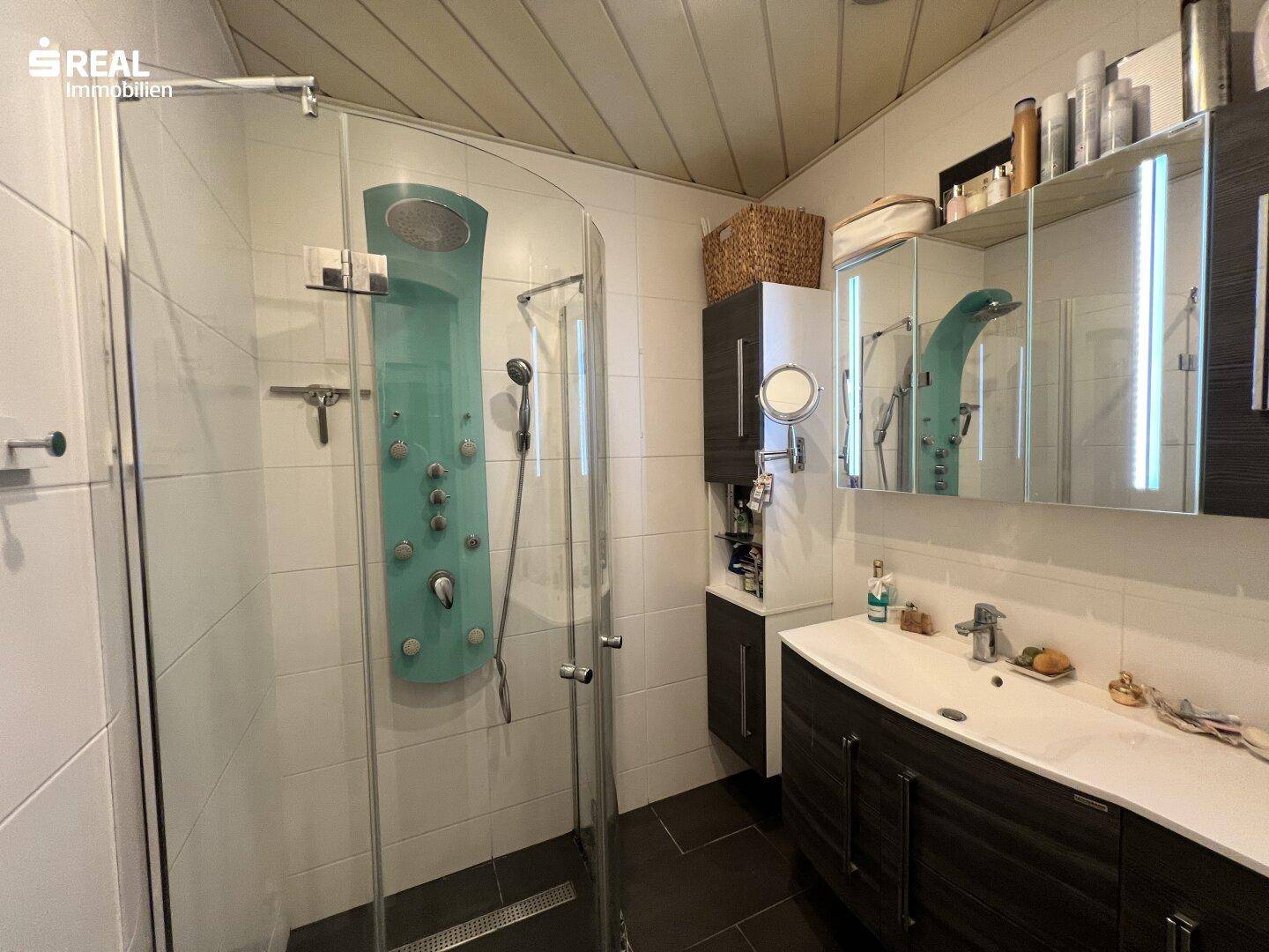 Modernes Badezimmer mit großer Duschkabine, Waschtisch und Spiegelschrank.