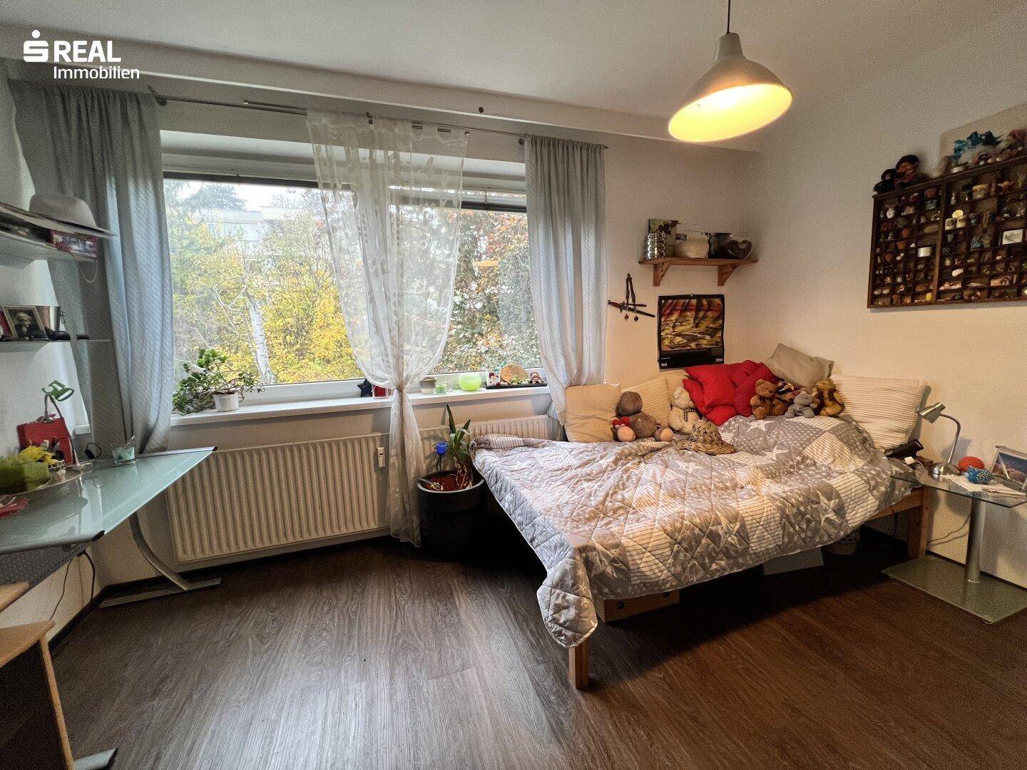 Helles Schlafzimmer mit Einzelbett, Schreibtisch und Blick ins Grüne.