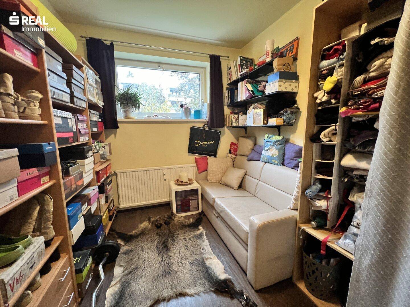 Vielseitiger Raum mit Regalen, Sofa und Fenster, ideal als Ankleide oder Büro.