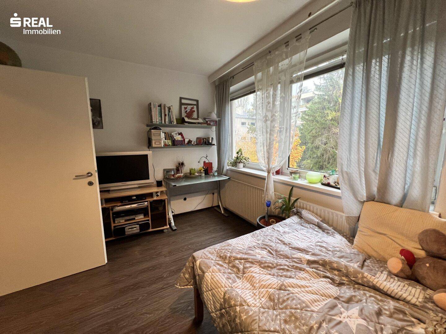 Helles Schlafzimmer mit Bett, Schreibtisch und Blick auf die umliegende Natur.