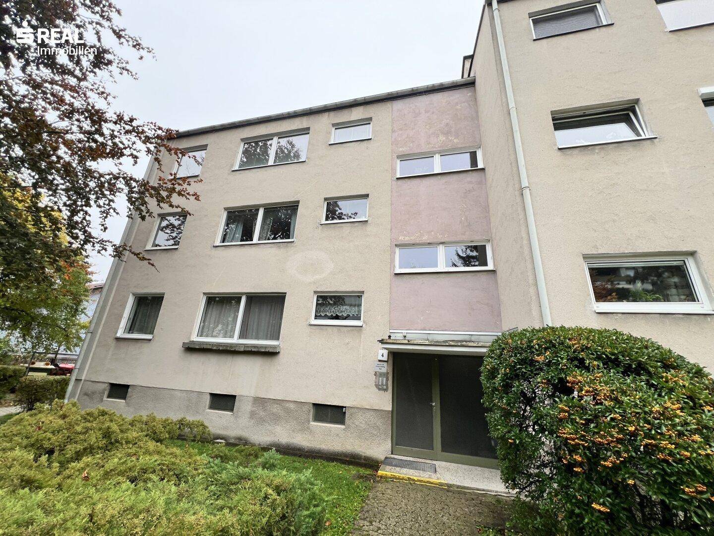 Die Vorderseite des Mehrfamilienhauses mit Eingangsbereich und gepflegter Hecke.