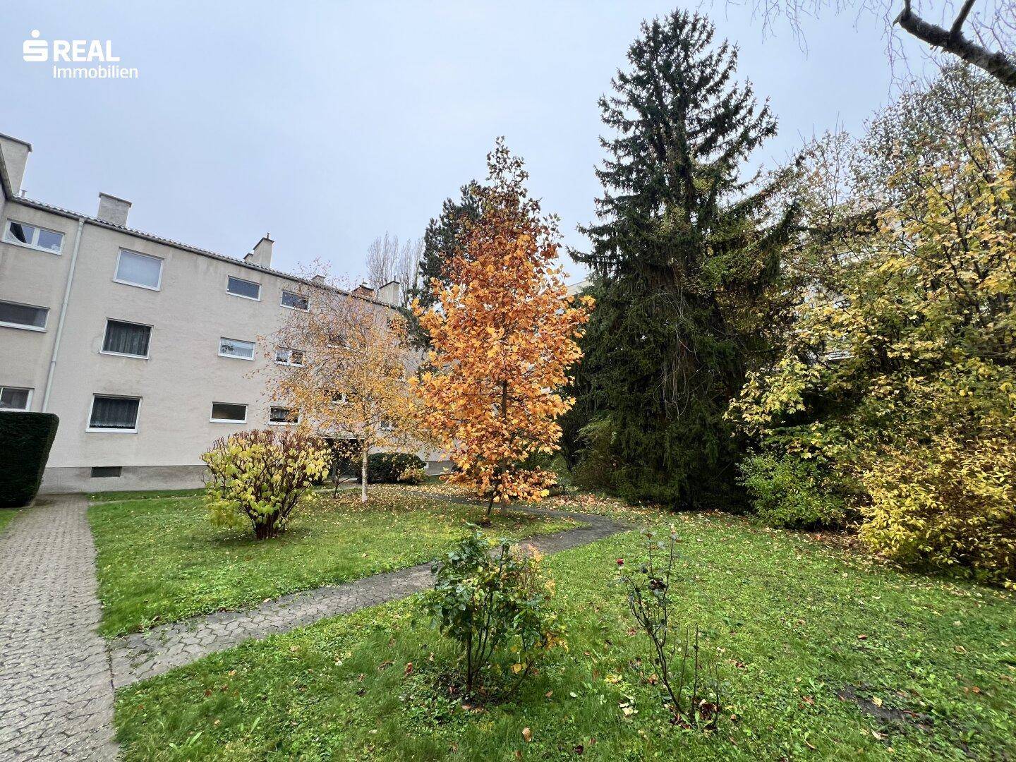 Gepflegter Gemeinschaftsgarten mit Rasenflächen, Bäumen und Wegen zwischen den Gebäuden.