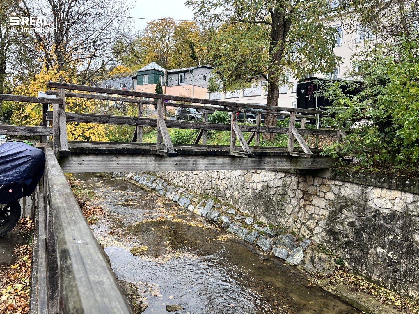 Holzbrücke über einen kleinen Bachlauf, umgeben von herbstlicher Natur.
