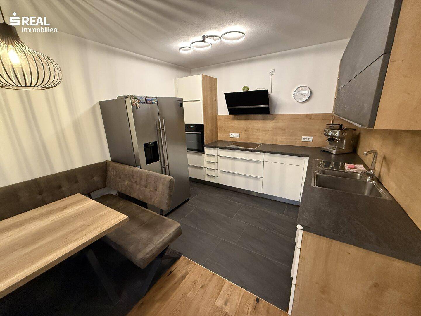 Moderne Einbauküche mit integriertem Essbereich, Edelstahlgeräten und dunklen Fliesen.