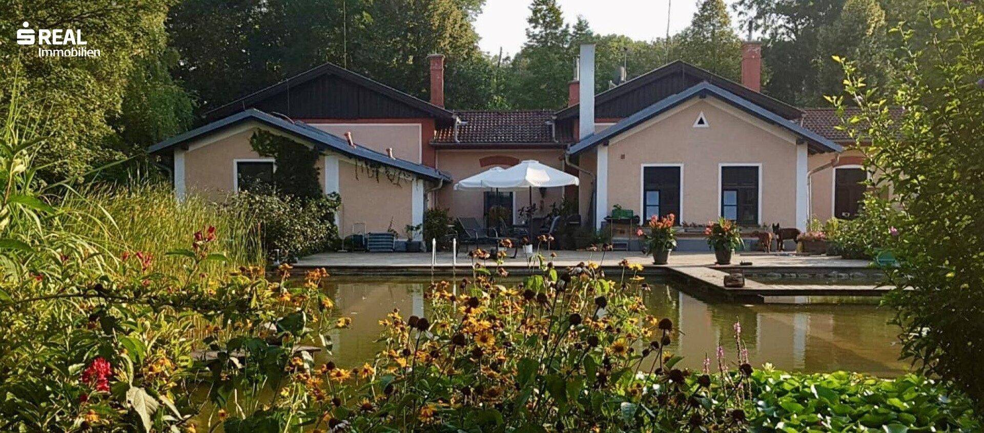 Charmantes Haus mit Teich, üppiger Bepflanzung und einer Terrasse mit Sonnenschirm.