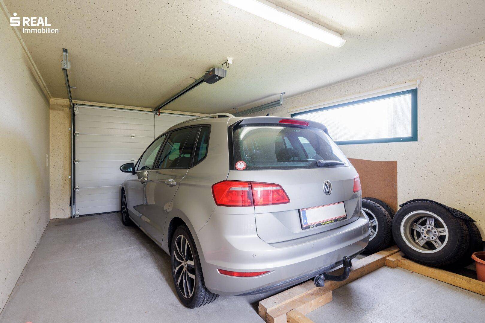 Geräumige Garage mit einem Fahrzeug und zusätzlichen Reifen, bietet sicheren Stellplatz.