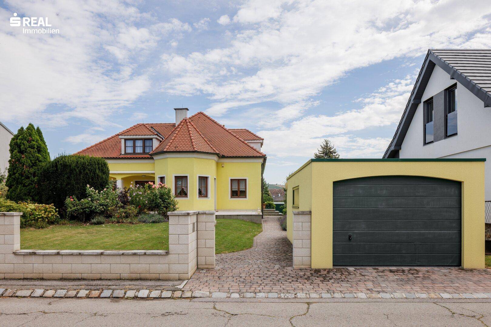 Gesamtansicht des Anwesens mit dem gelben Haupthaus, gepflasterter Auffahrt und separater Garage.