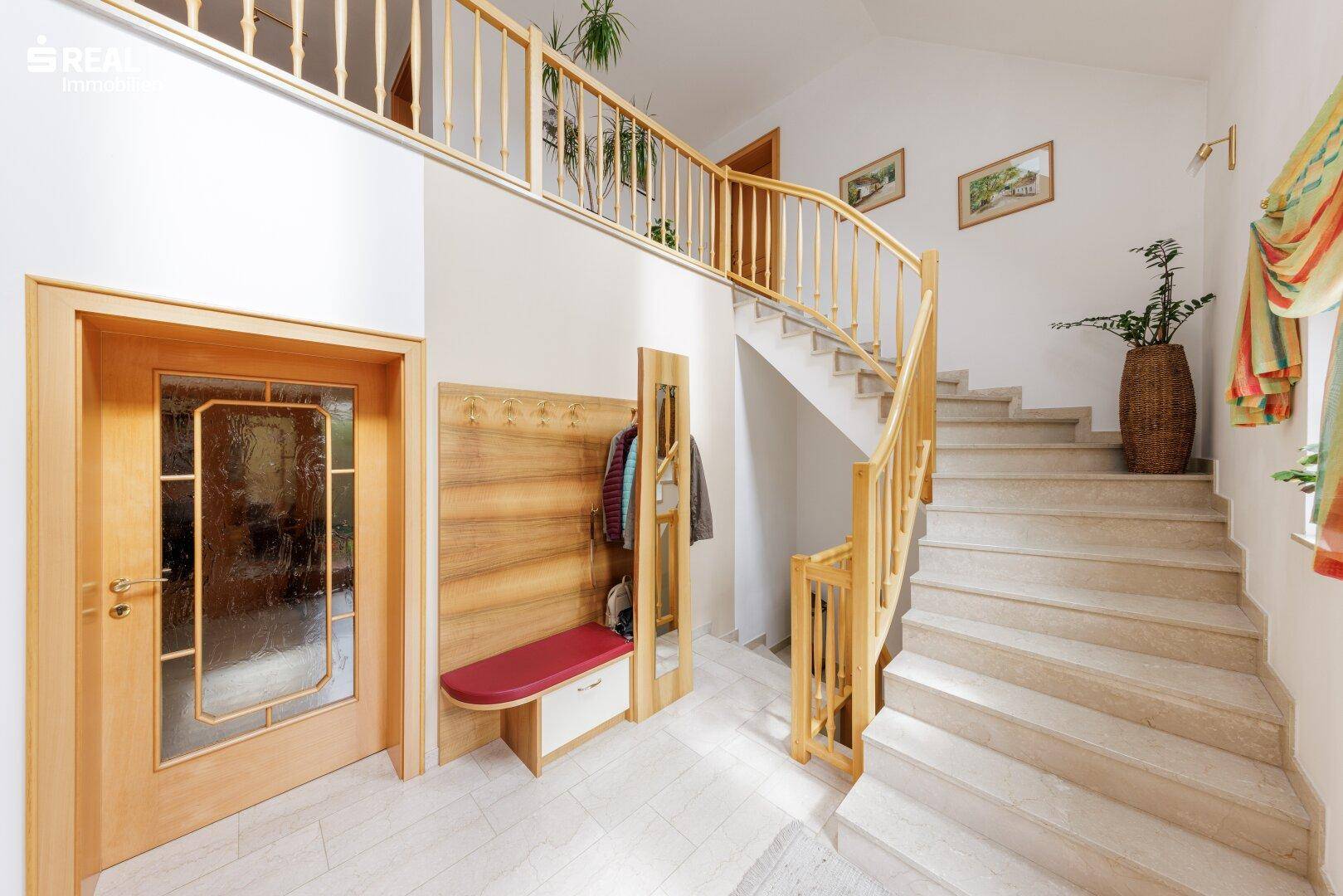 Heller Eingangsbereich mit Natursteinboden, Holztreppe und Galerie, die zu den oberen Etagen führt.