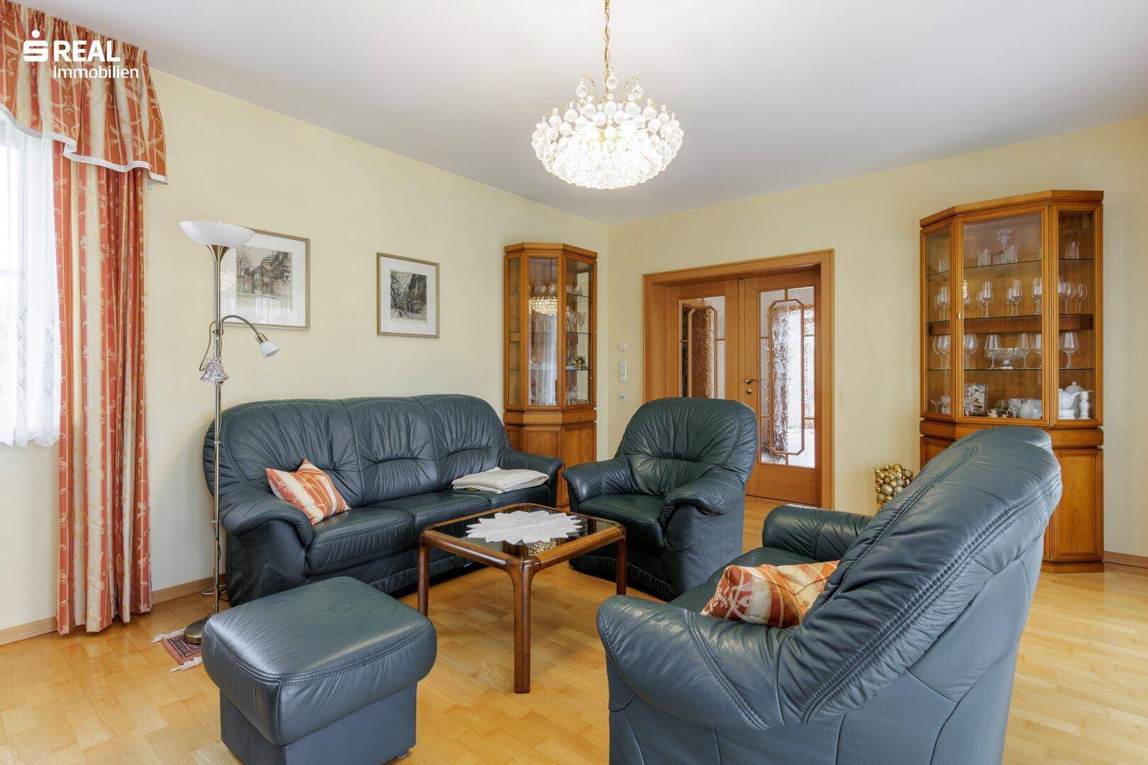 Klassisches Wohnzimmer mit bequemen Ledersofas, Parkettboden und einem eleganten Kronleuchter.