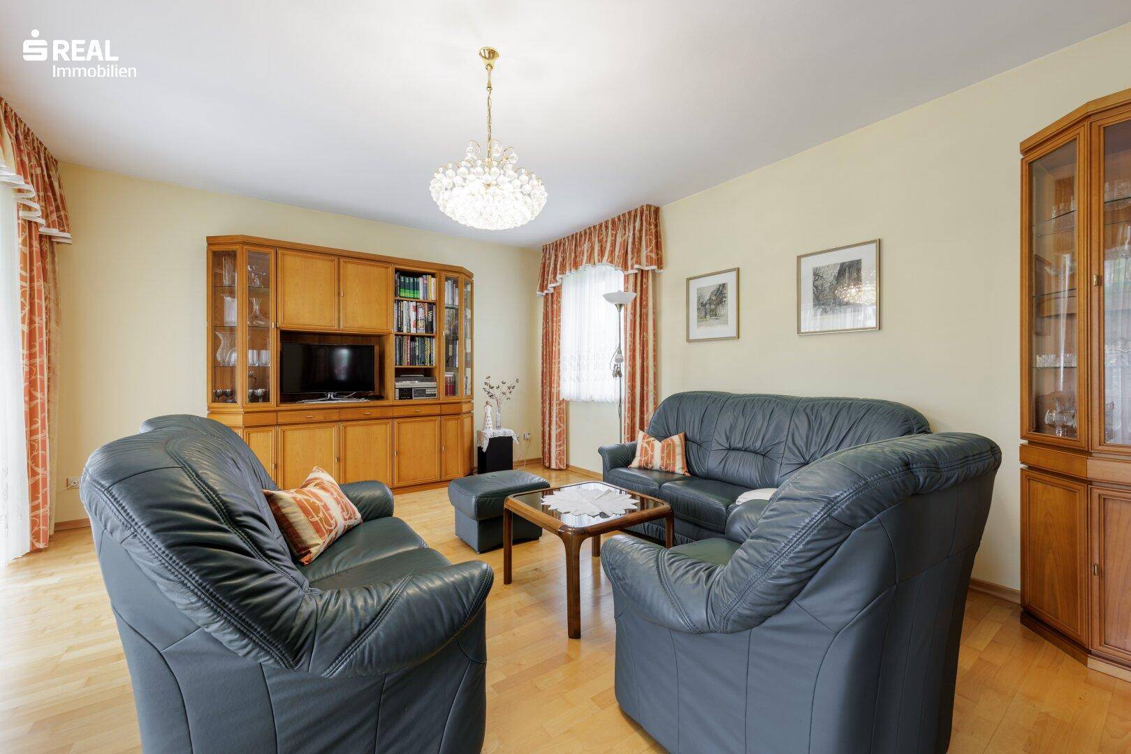 Gemütliches Wohnzimmer mit Ledersitzgruppe, Holzschränken und einem Kronleuchter, ideal für entspannte Abende.