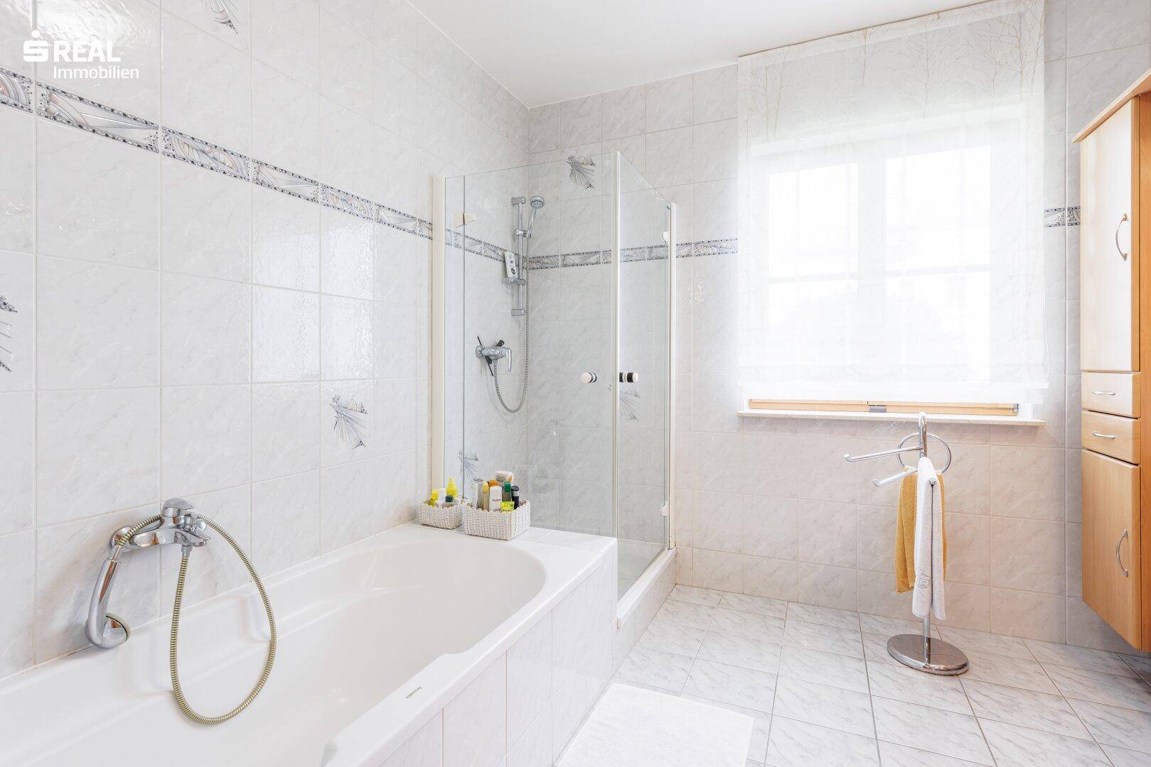 Geräumiges Badezimmer mit Badewanne, separater Dusche und Fenster, hell gefliest.
