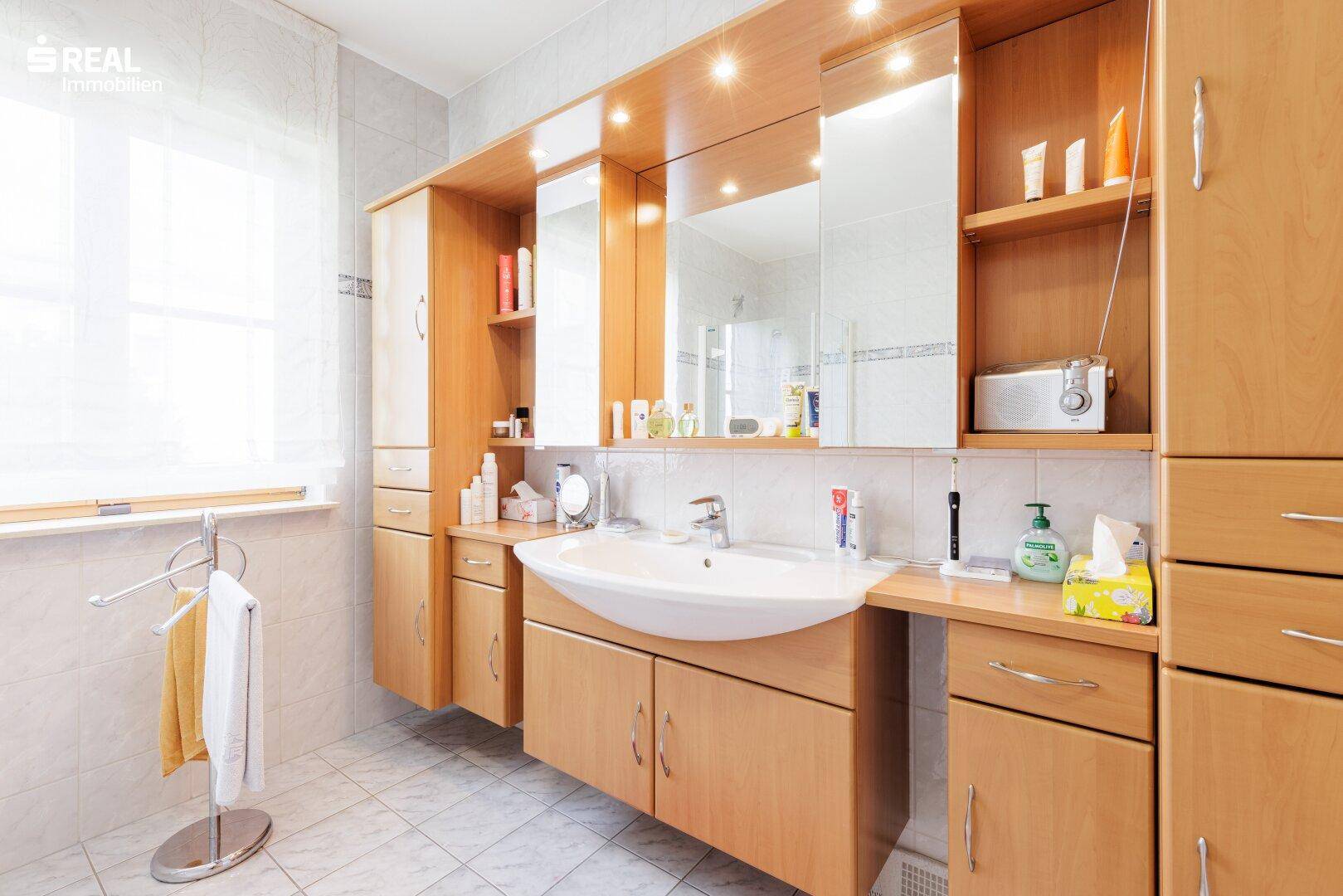Modernes Badezimmer mit großem Waschtisch, Spiegelschrank und viel Stauraum in Holzoptik.