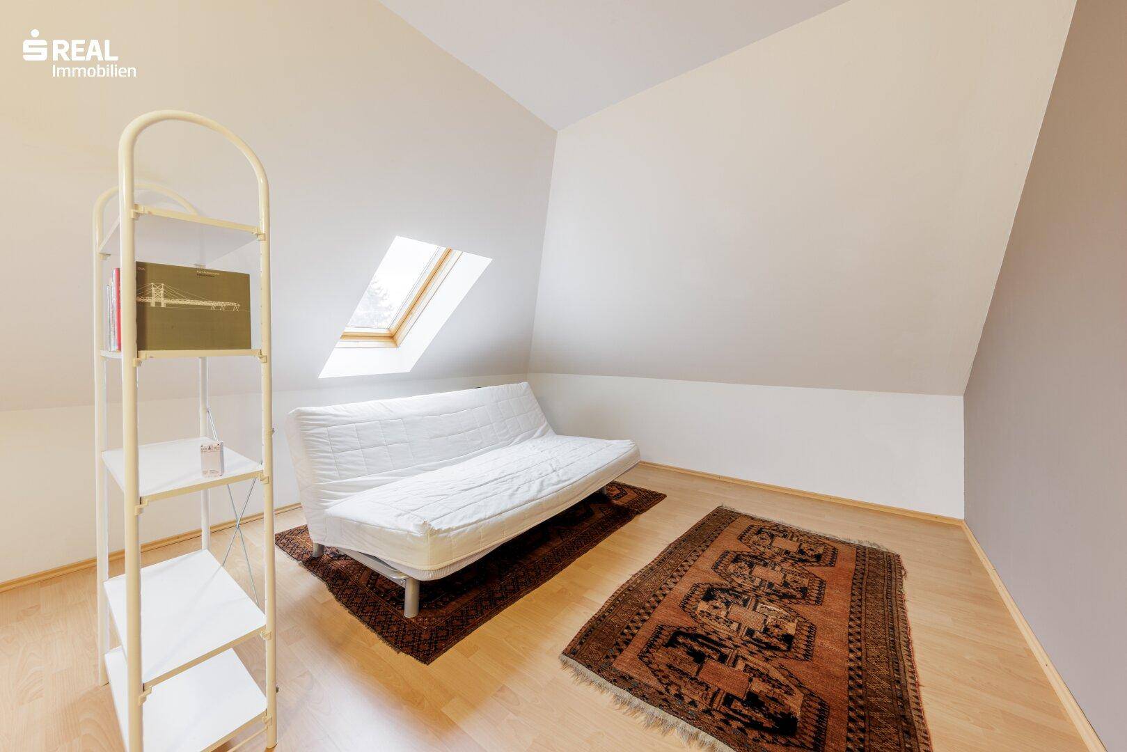 Gemütlicher Dachbodenraum mit Dachfenster, Parkettboden und Schlafsofa, ideal als Gästezimmer.
