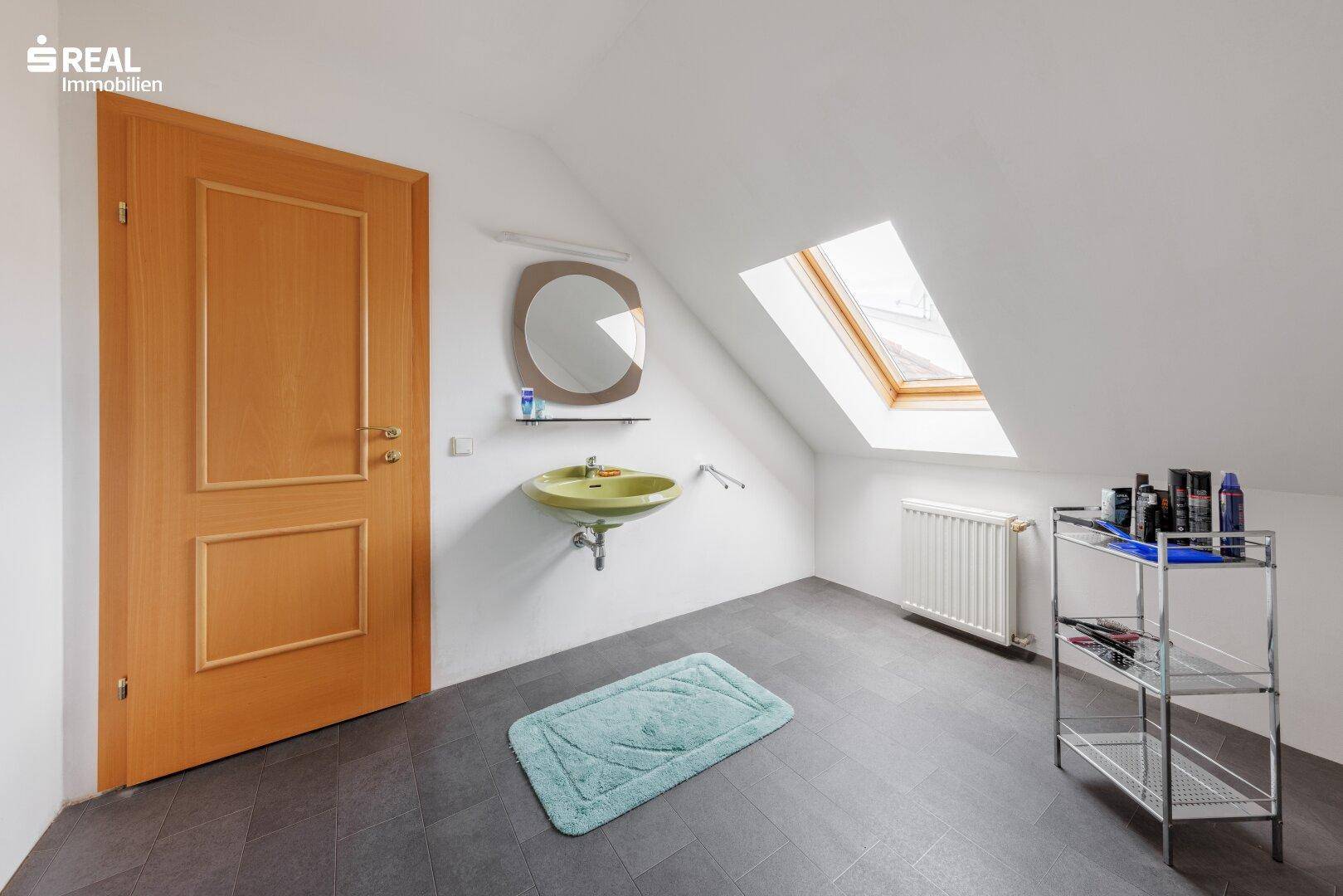 Kleines Badezimmer im Dachgeschoss mit Dachfenster, Waschtisch und dunklem Fliesenboden.