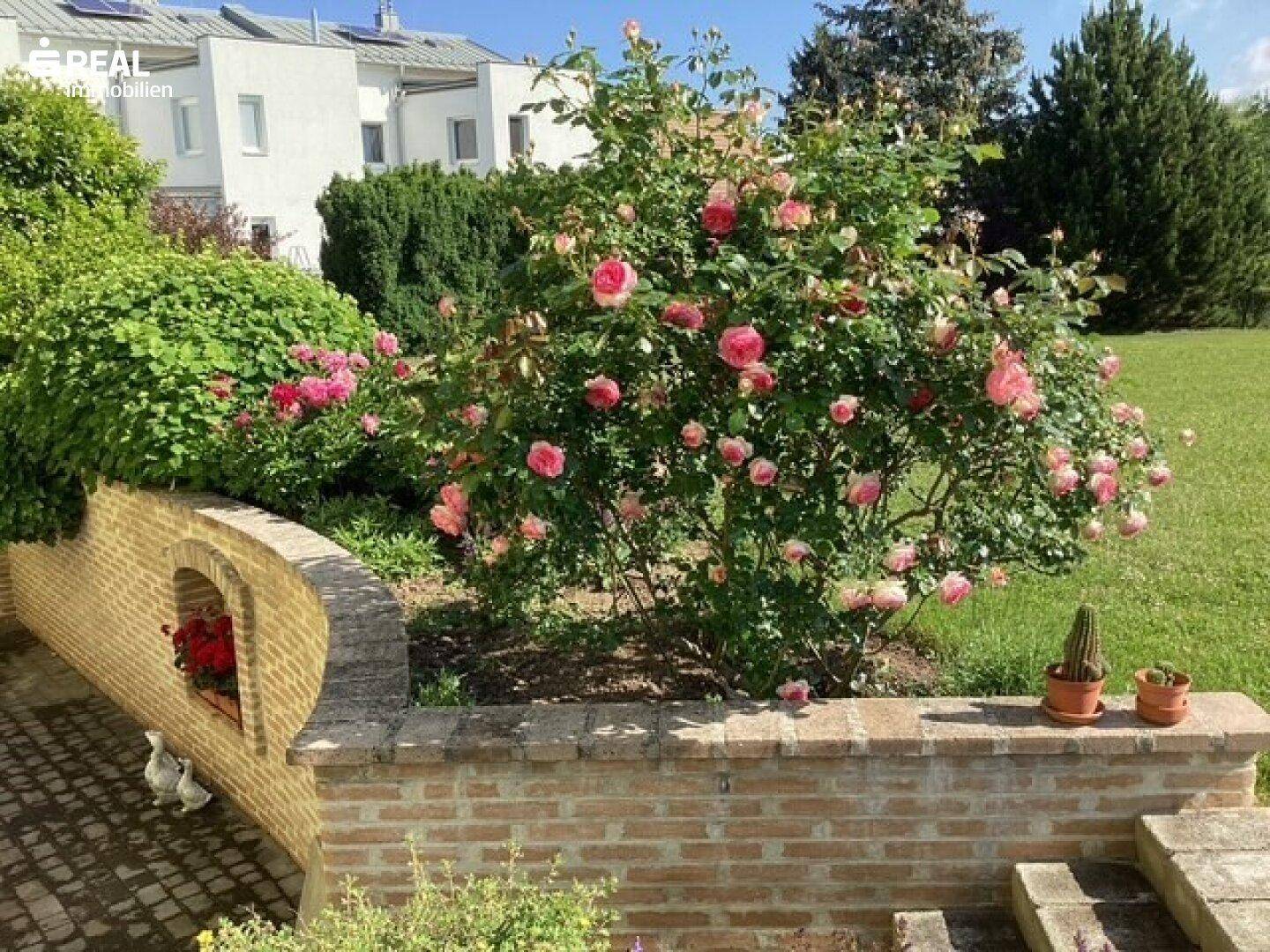 Erhöhtes Blumenbeet mit blühenden Rosen und einer dekorativen Ziegelmauer im Gartenbereich.