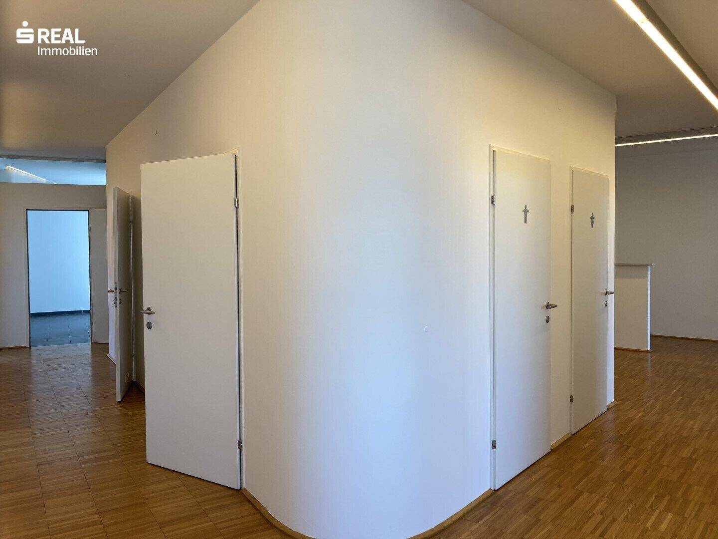 Heller Flurbereich mit mehreren Türen, wahrscheinlich zu Toiletten oder Nebenräumen, und Holzparkettboden.