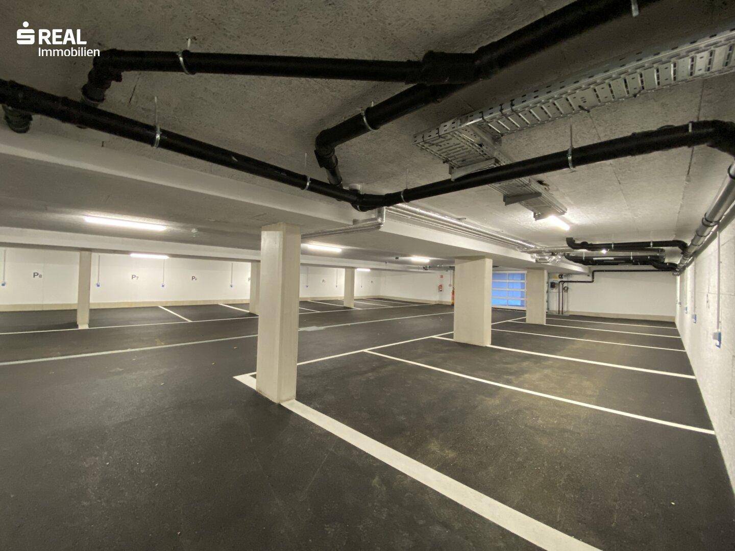 Geräumige Tiefgarage mit vielen markierten Stellplätzen und sichtbaren Installationen an der Decke.