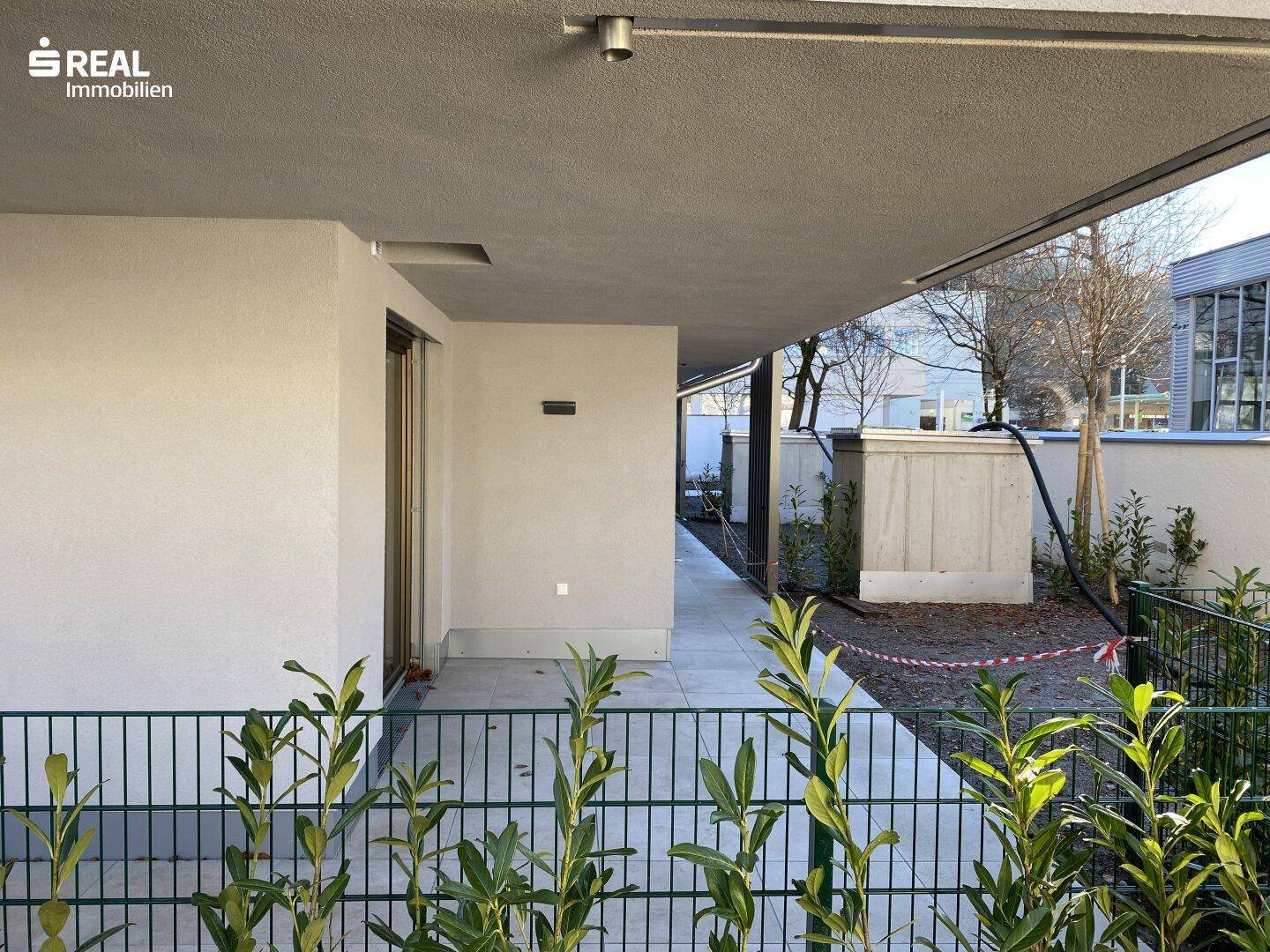 Überdachter Außenbereich im Erdgeschoss, der als Terrasse dient und Zugang zu einem kleinen Gartenabschnitt bietet.
