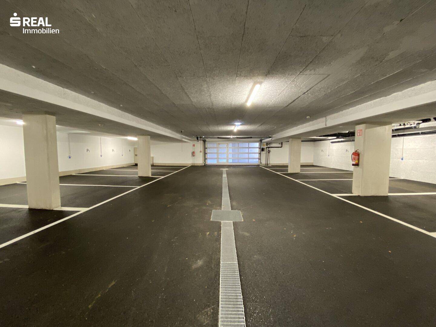 Geräumige Tiefgarage mit markierten Stellplätzen und Zufahrtstor in einem Neubau.