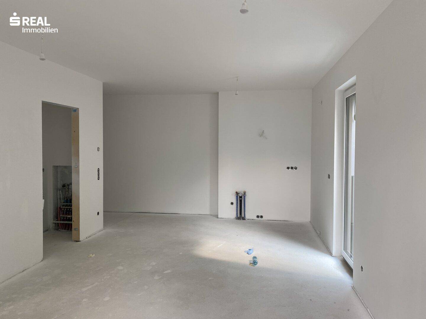 Unfertiger Innenraum mit weißen Wänden und rohem Betonboden, bereit für den Ausbau.