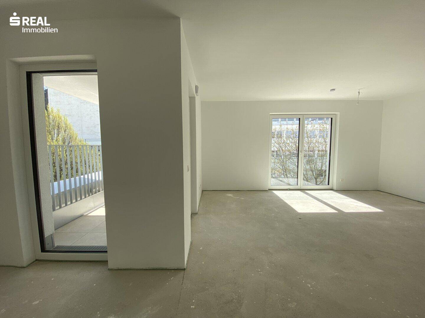 Heller, unmöblierter Wohnbereich mit großen Fenstern und Zugang zu einem Balkon, bereit für den Ausbau.