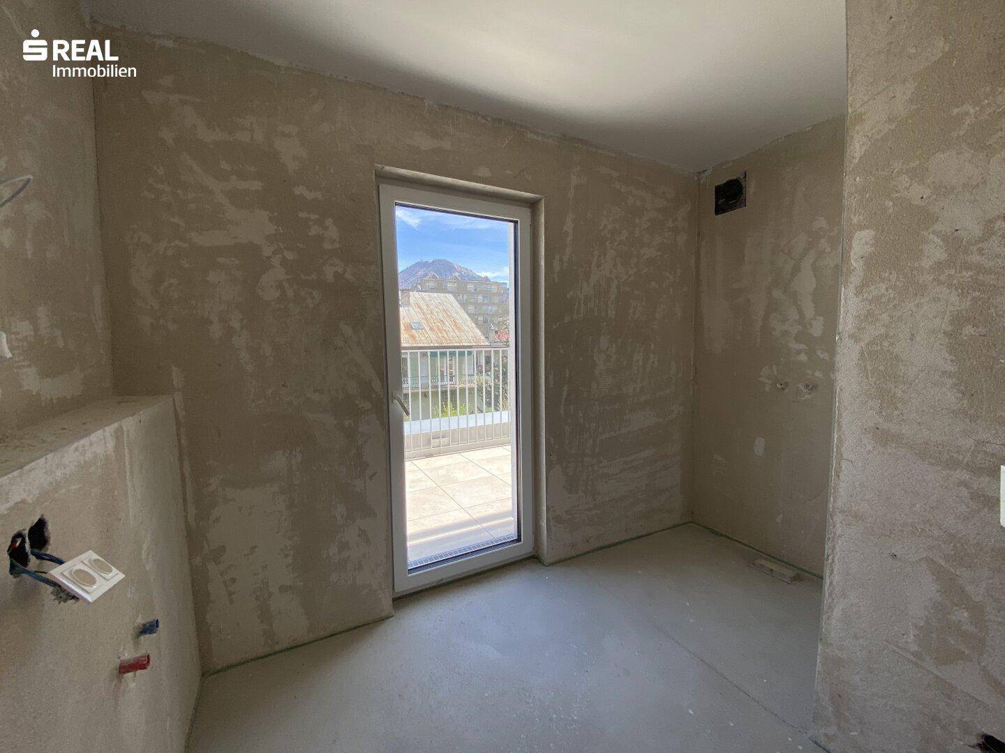 Unfertiger Raum mit Zugang zu einer Terrasse und Blick auf die Umgebung, wartet auf den Innenausbau.