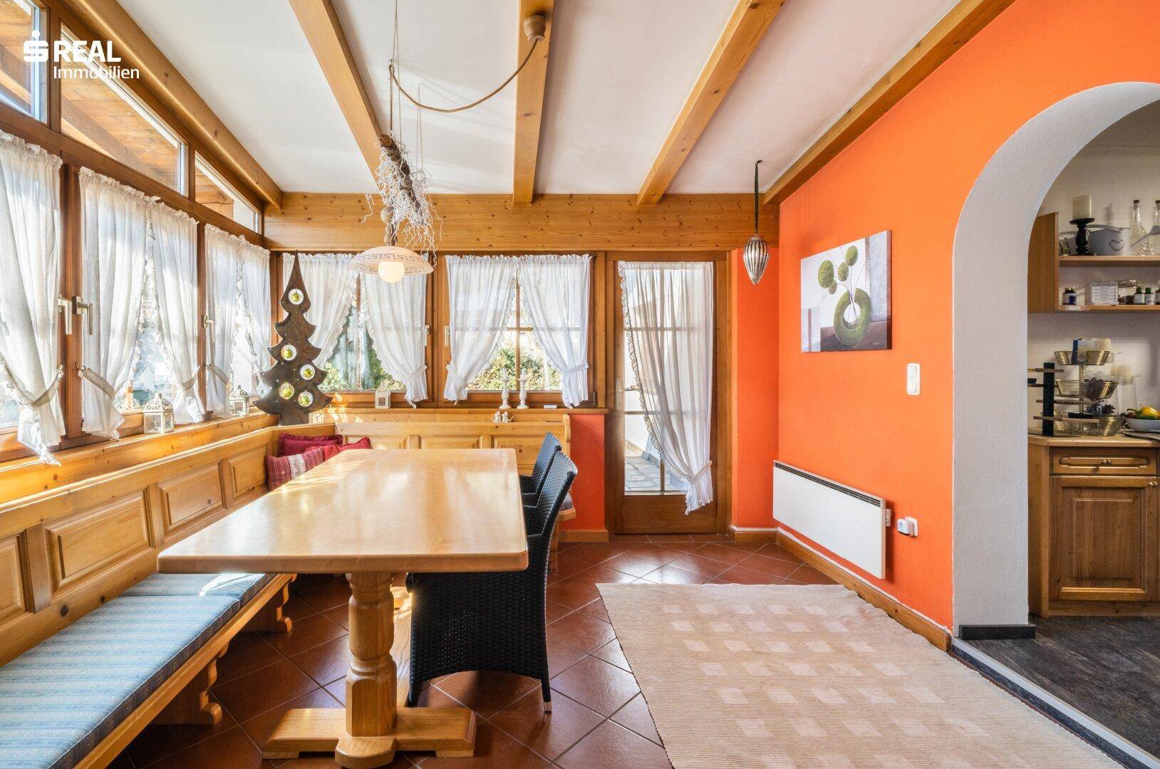 Gemütlicher Essbereich mit Holzbalken, orangefarbenen Wänden und Zugang zur Küche.