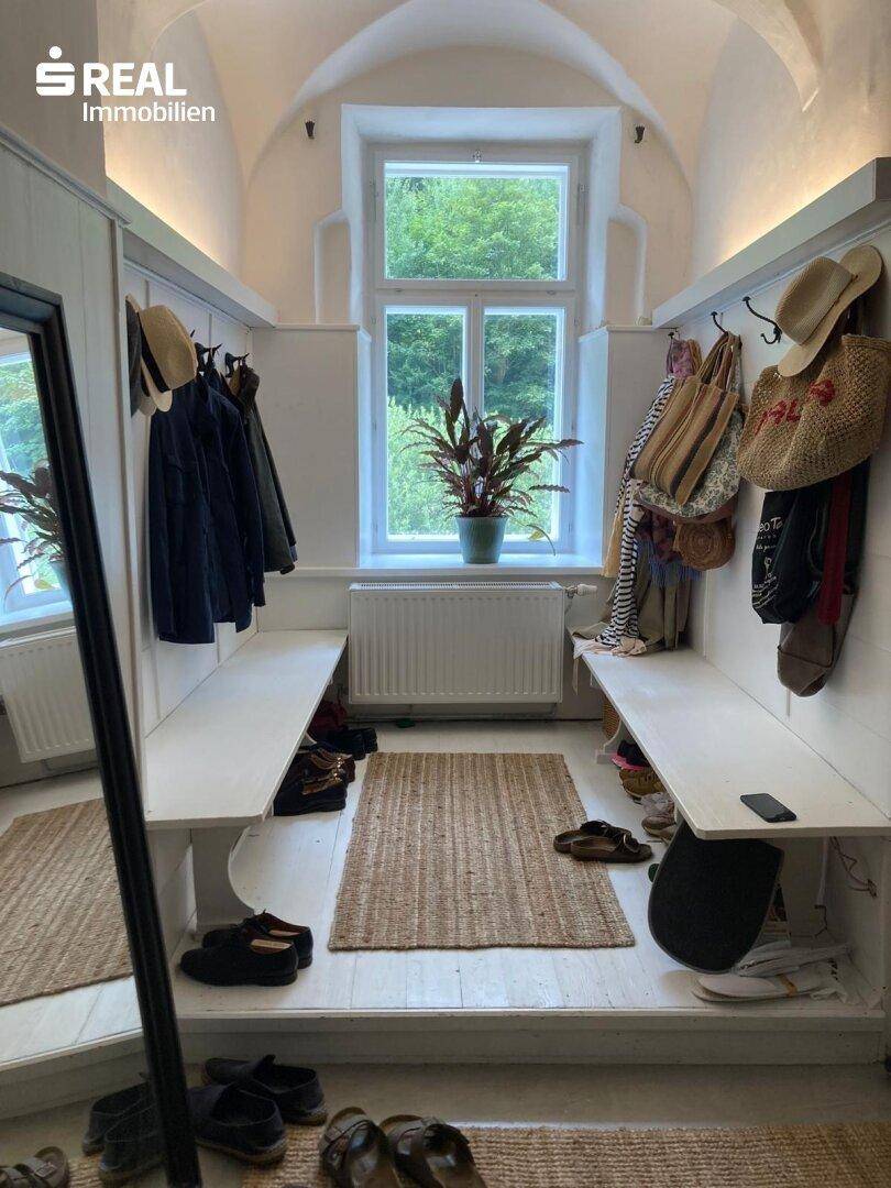 Heller Flur mit Sitzbänken, Garderobe und einem großen Fenster, das viel Tageslicht hereinlässt.