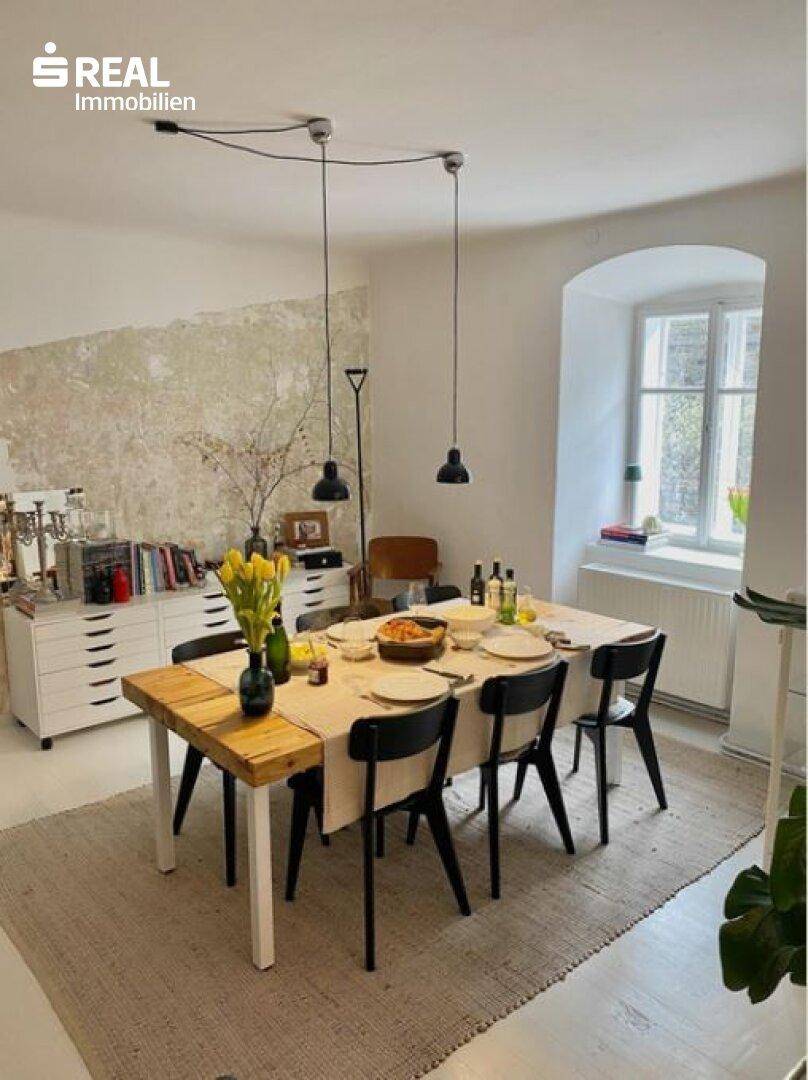 Heller Essbereich mit Holztisch und Stühlen, einer strukturierten Wand und natürlichem Lichteinfall.