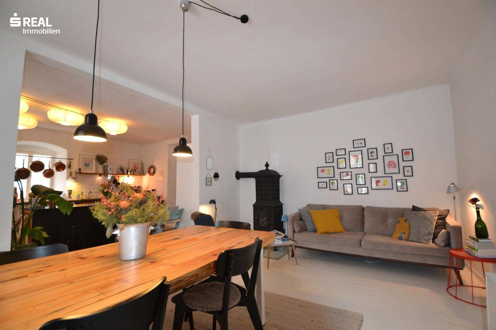 Gemütlicher Wohn- und Essbereich mit einem Sofa, Holztisch und einem traditionellen Kachelofen.