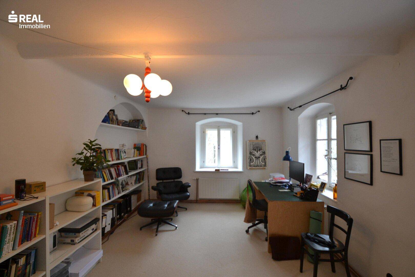 Helles Arbeitszimmer mit Bücherregalen, Schreibtisch und mehreren Fenstern für viel Tageslicht.
