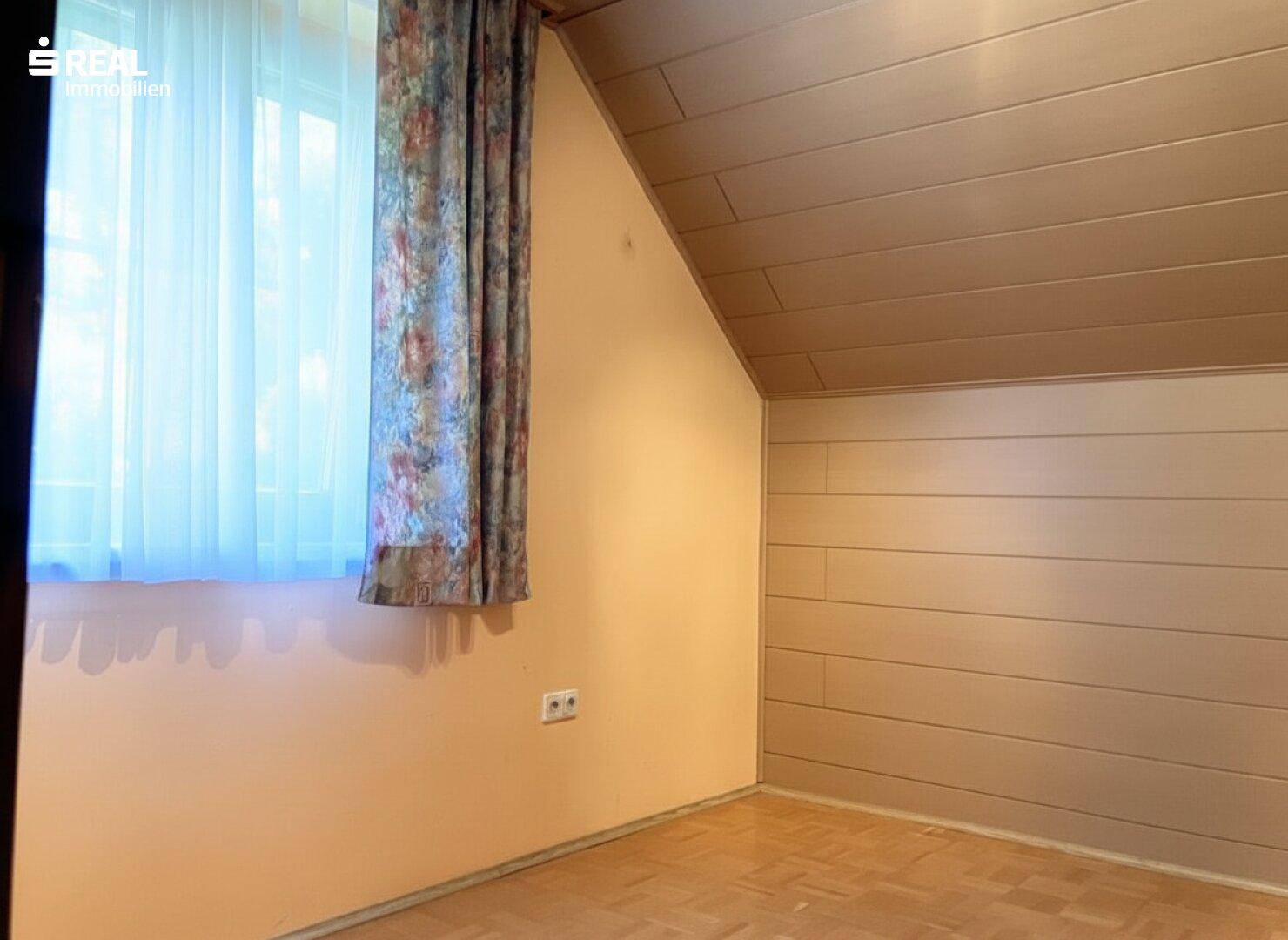 Gemütliches Zimmer im Dachgeschoss mit Holzverkleidung an der Wand und schrägen Decken.