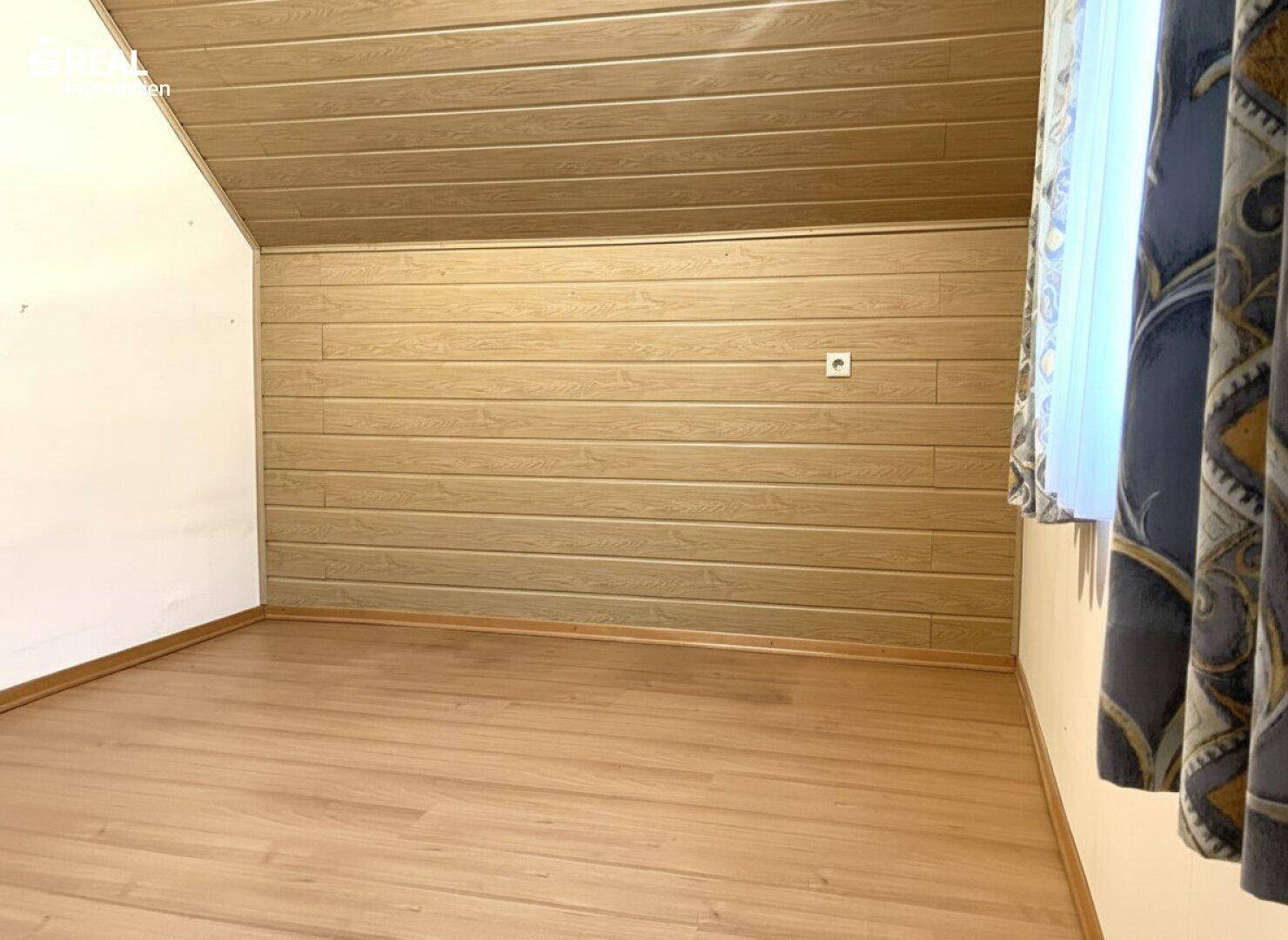 Helles Schlafzimmer im Dachgeschoss mit Laminatboden und holzverkleideten Wänden unter der Schräge.