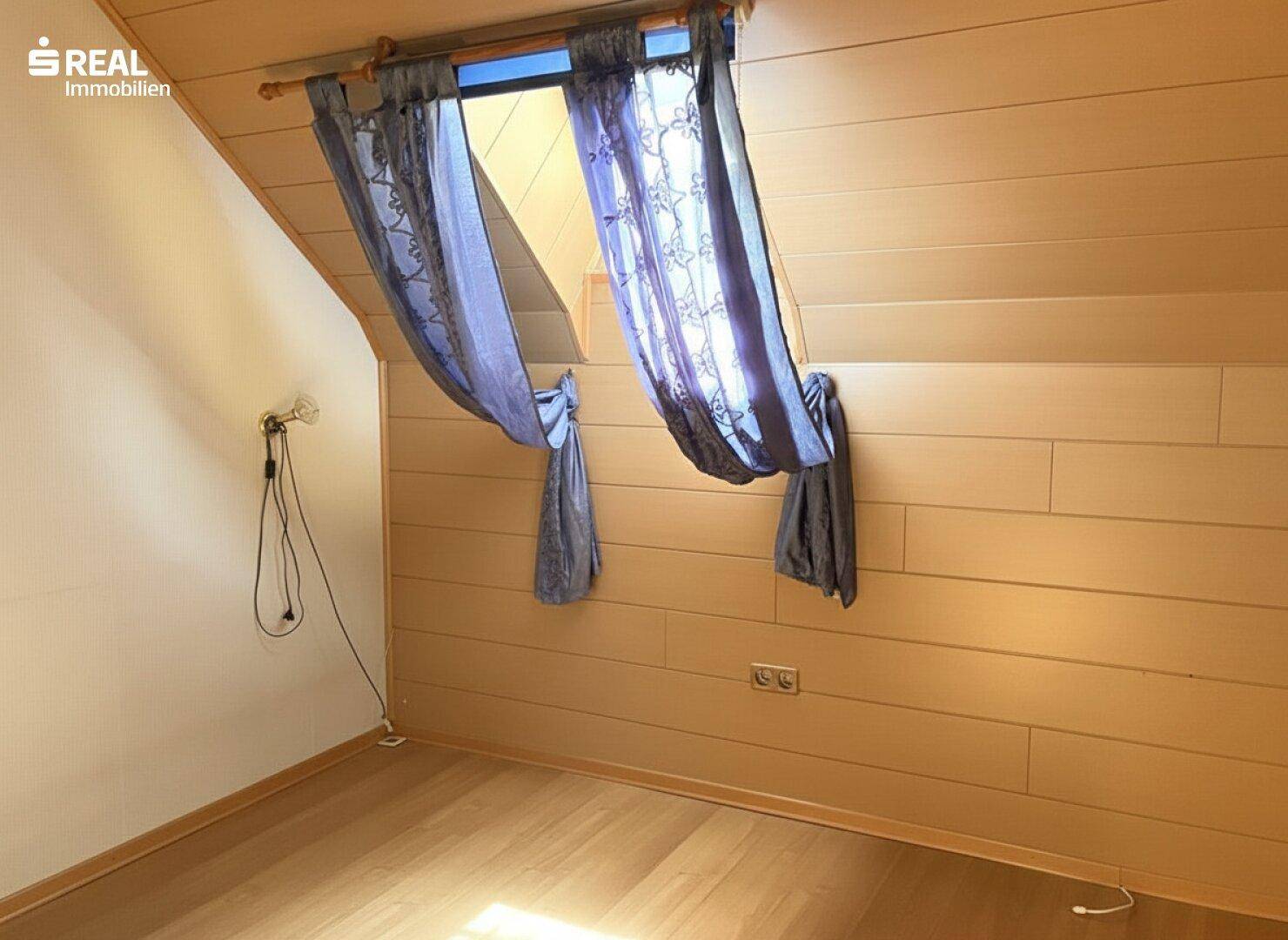 Dachgeschosszimmer mit Laminatboden, Holzverkleidung und einem Dachfenster für natürliches Licht.