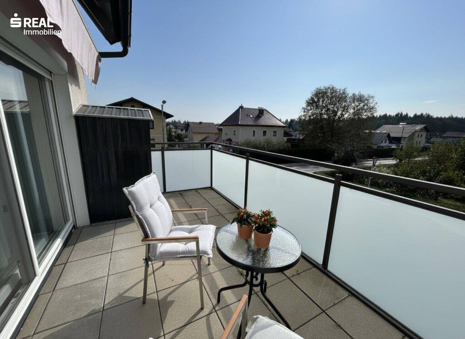 Sonniger Balkon mit Fliesenboden, Glasbrüstung und Blick auf die Umgebung.