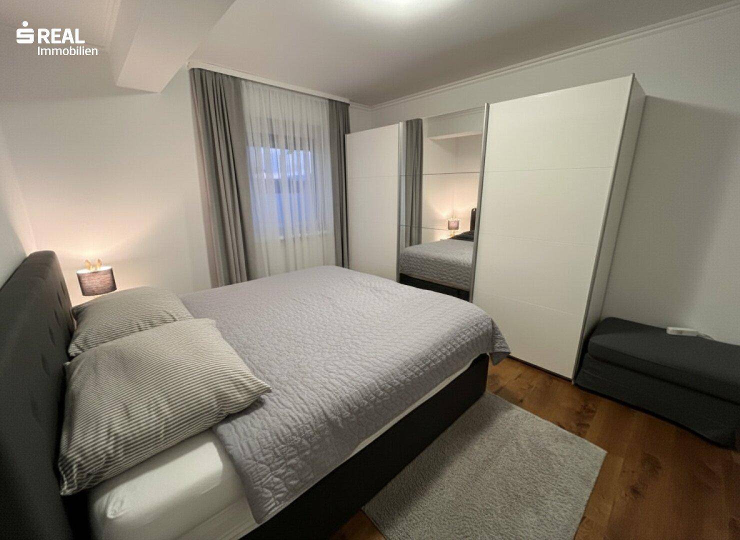 Schlafzimmer mit Holzboden, großem Bett und Spiegelschränken.