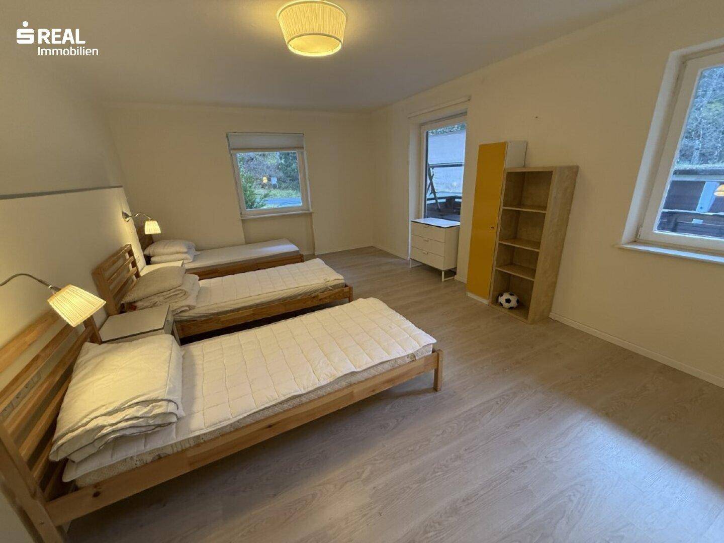 Geräumiges Schlafzimmer mit drei Einzelbetten, Holzboden und mehreren Fenstern mit Ausblick.