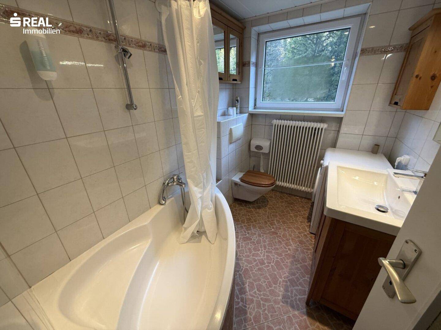 Traditionelles Badezimmer mit Badewanne, WC, Waschtisch und Fenster, gefliesten Wänden und Boden.