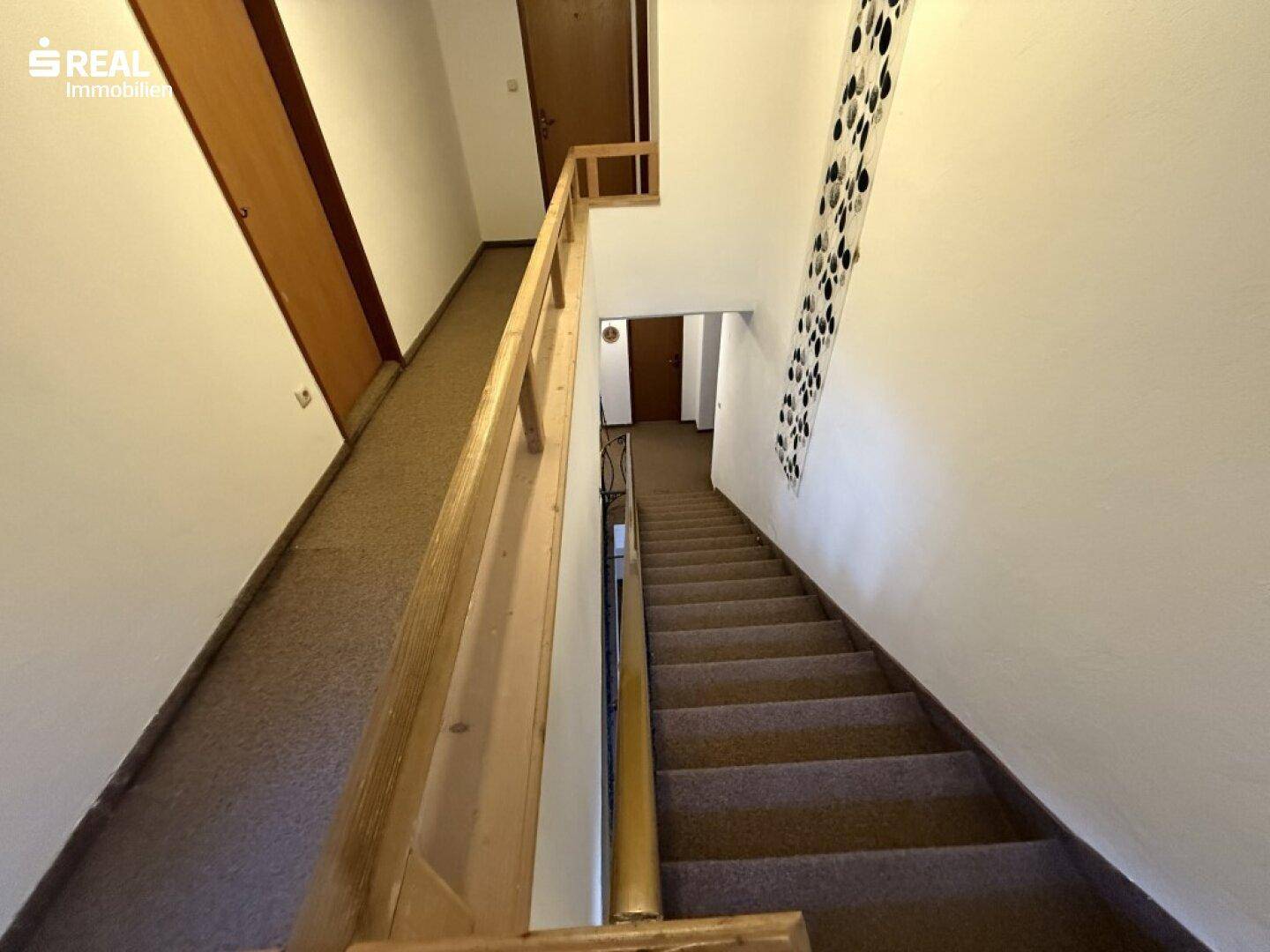 Treppenhaus mit Teppichstufen und Holzgeländer, das die verschiedenen Etagen des Hauses verbindet.
