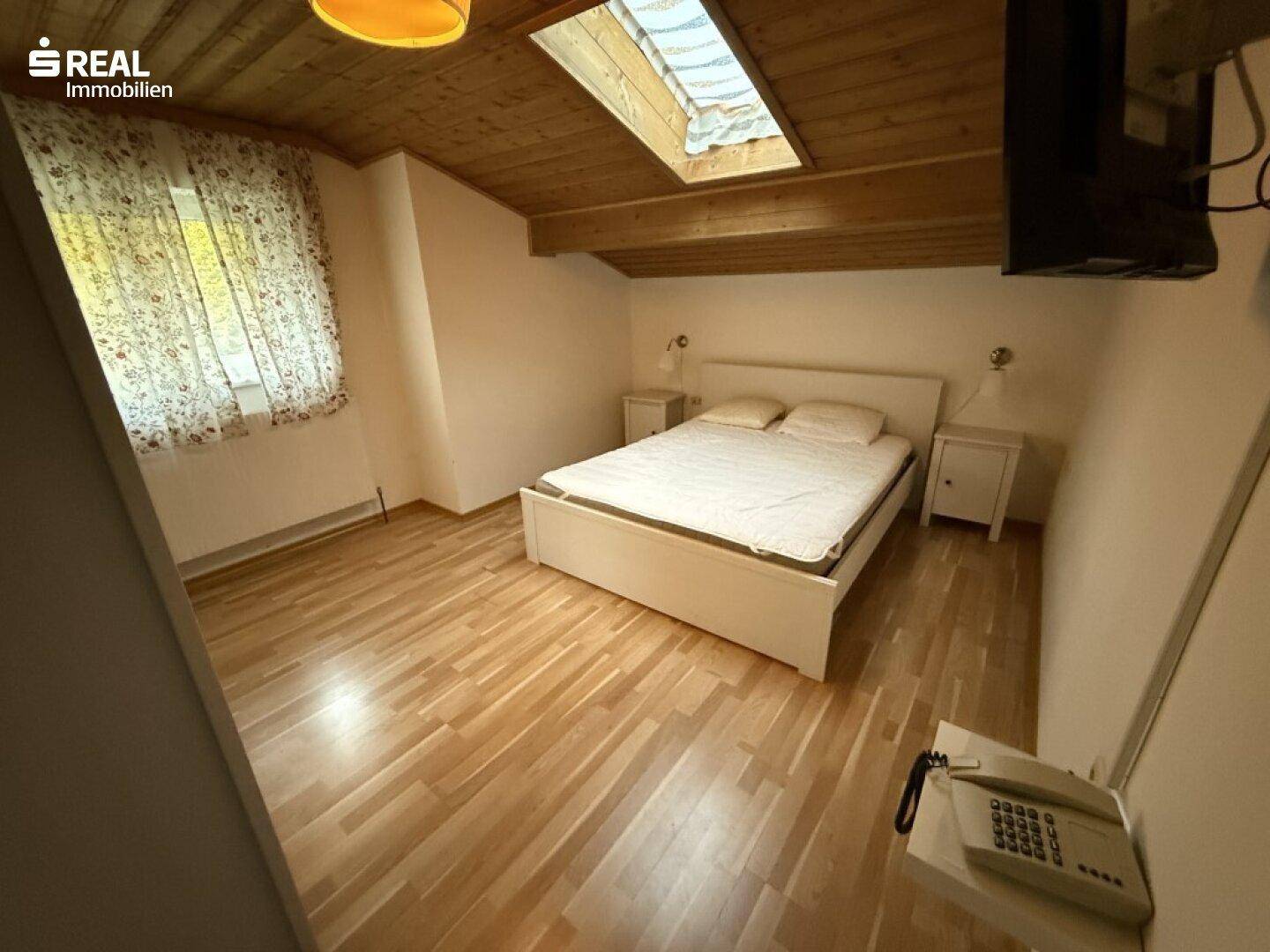 Schlafzimmer mit Doppelbett, Holzbalkendecke, Holzboden und einem Dachfenster für natürliches Licht.