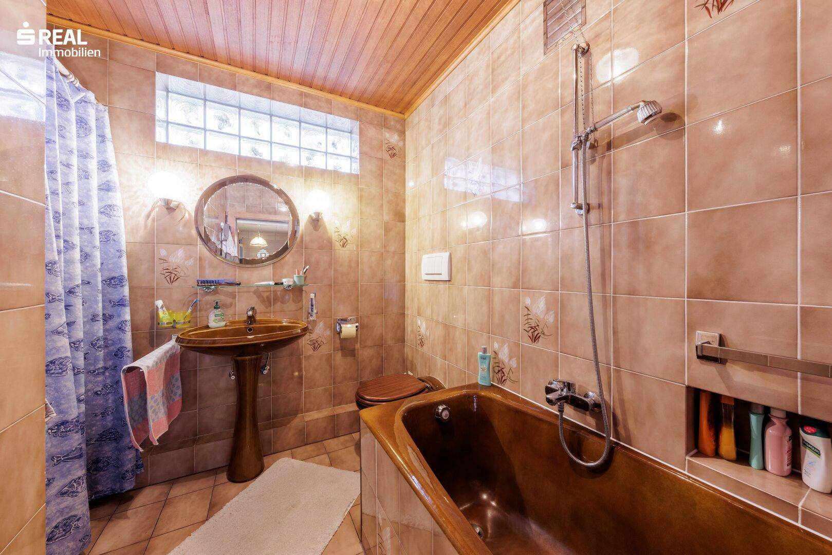 Traditionelles Badezimmer mit braunen Fliesen, Badewanne und Holzdecke, ausgestattet mit Dusche.