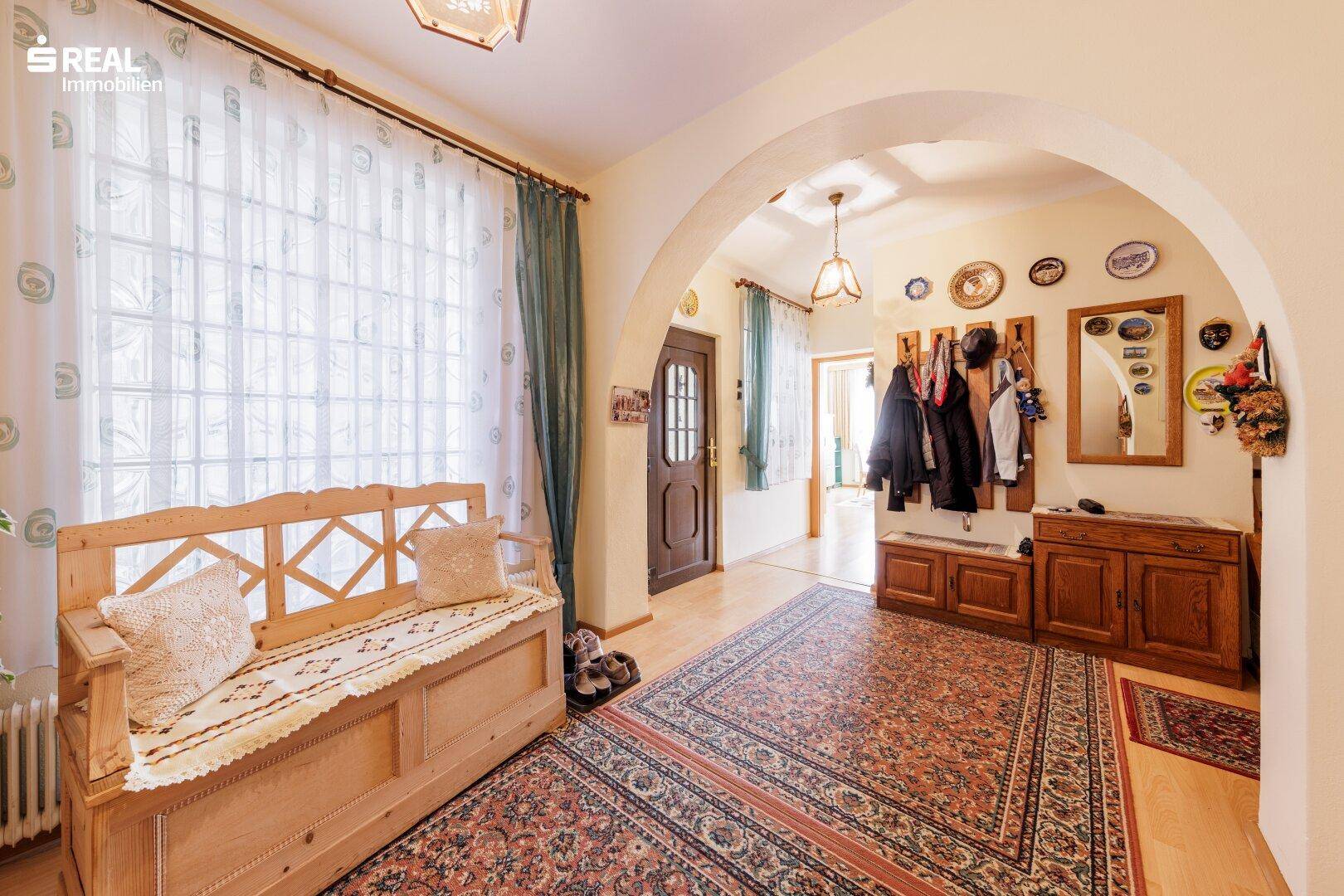 Geräumiger Eingangsbereich mit traditionellen Holzmöbeln, Teppichboden und viel Tageslicht durch große Fenster.