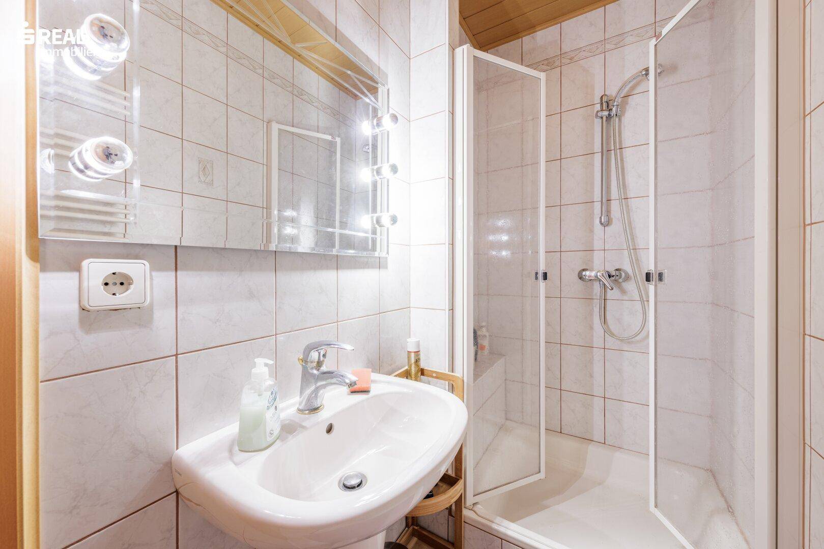 Modernisiertes Badezimmer mit weißen Fliesen, Dusche und Einzelwaschbecken.