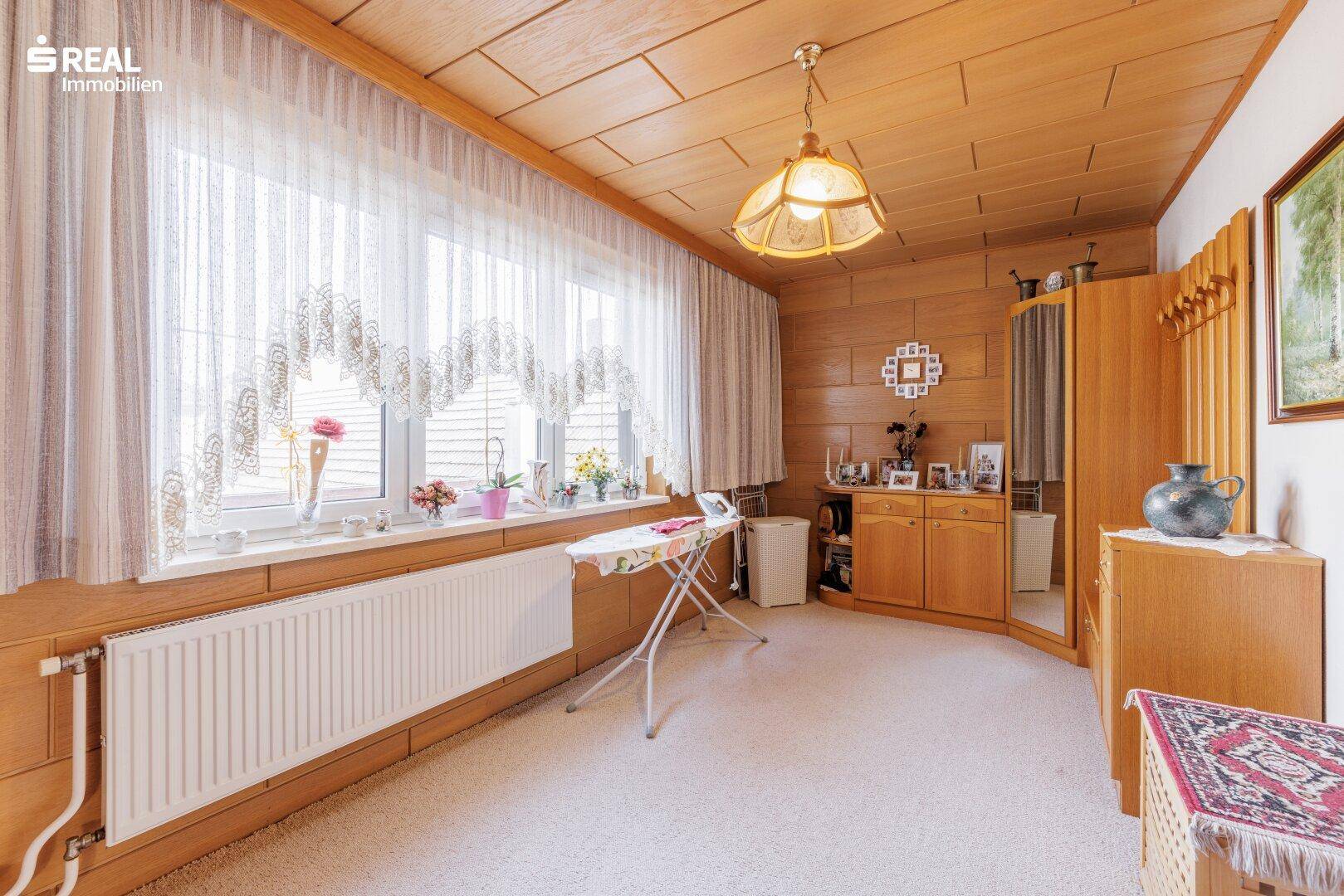 Raum mit Teppichboden, Holzvertäfelung und großem Fenster, vielseitig nutzbar.