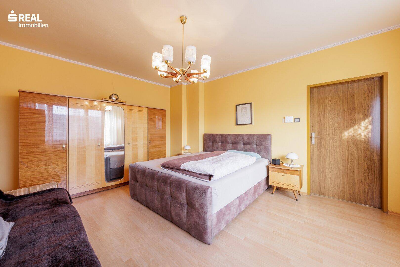 Helles Schlafzimmer mit Doppelbett, Laminatboden und großem Kleiderschrank.