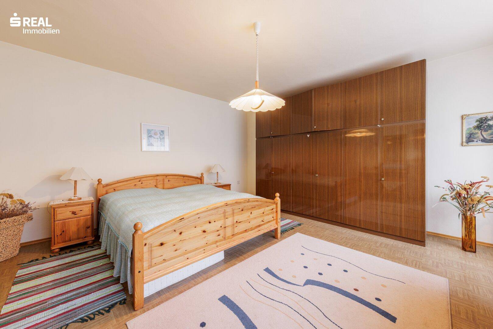 Schlafzimmer mit Doppelbett aus Holz, Laminatboden und großer Holzschrankwand.