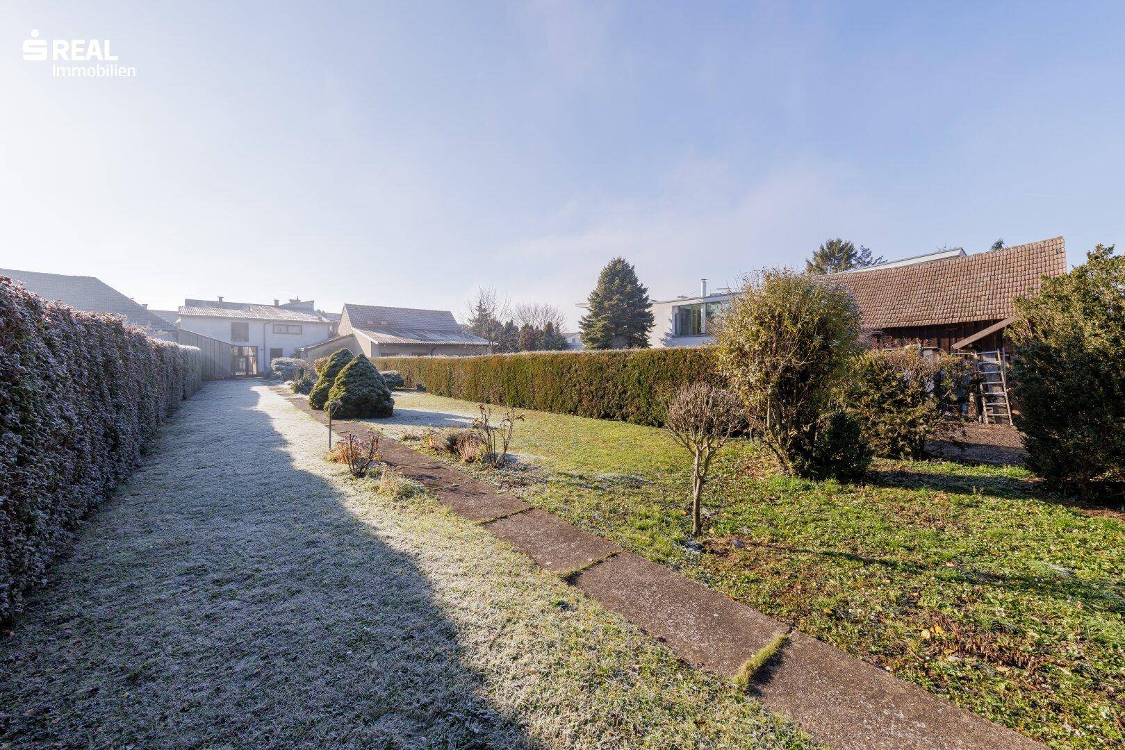Großer Gartenbereich mit Rasenfläche, Hecken und einem Weg, umgeben von Natur.