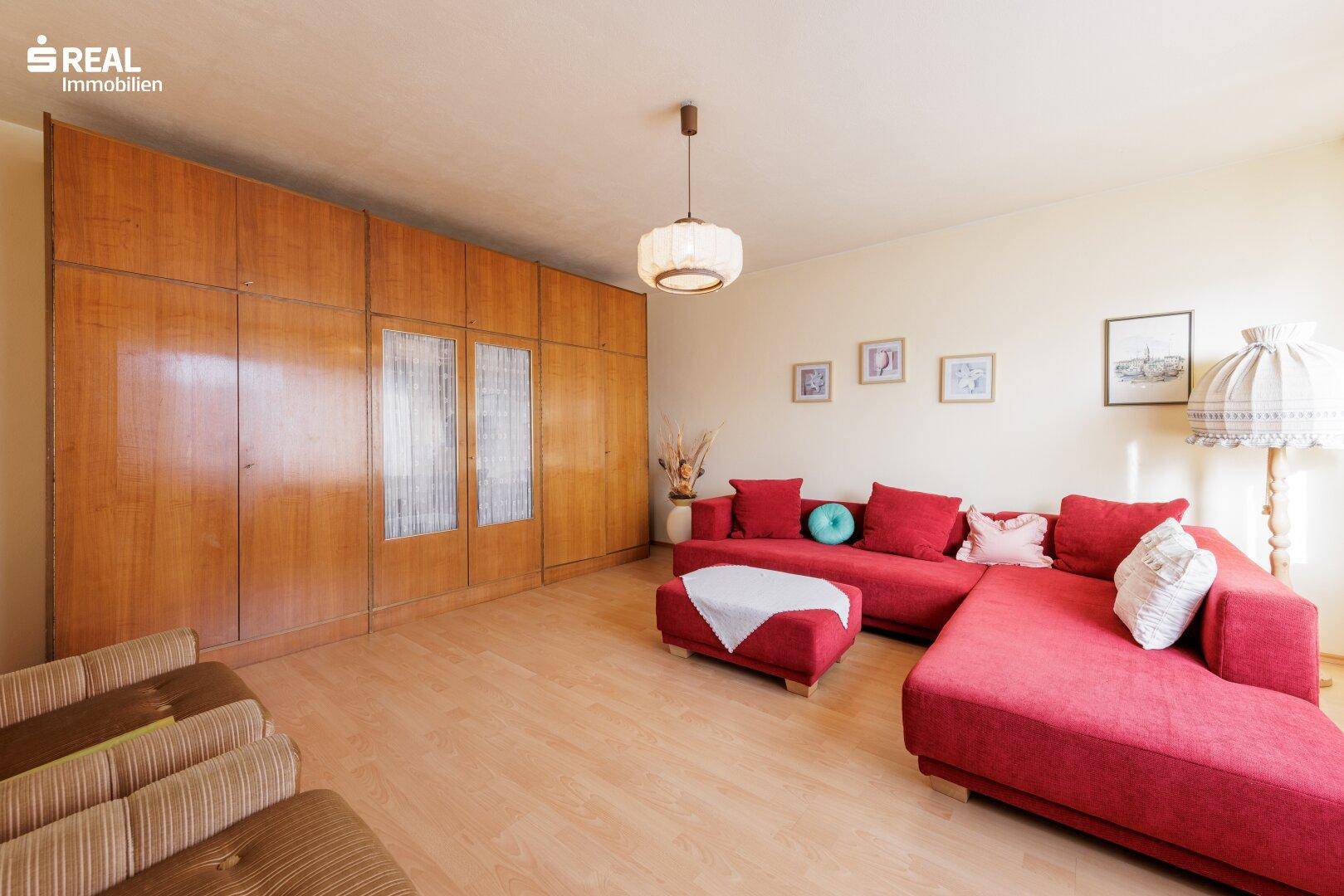 Geräumiges Wohnzimmer mit rotem Sofa, Laminatboden und großer Holzschrankwand.